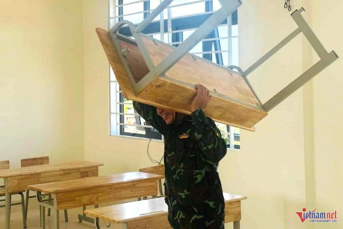 Bảo vệ nhà trường hỗ trợ khiêng bàn ghế vào lớp học. Ảnh: HVC