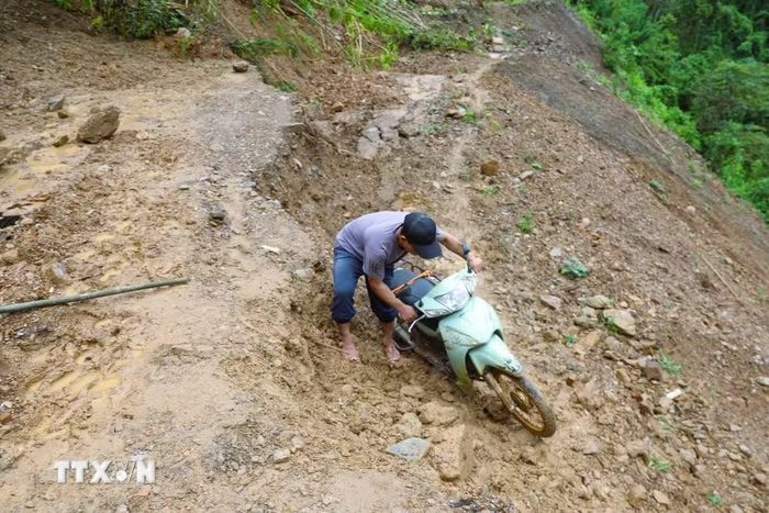 Người dân vất vả, khó khăn khi nỗ lực đưa xe máy qua điểm sạt lở trên tuyến đường Xốp Kho-Na Ngân (xã Nga My, Nghệ An). (Ảnh: Xuân Tiến/TTXVN)