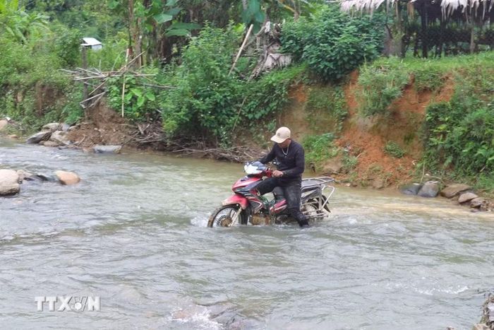 Người dân vất vả đưa xe máy qua đoạn suối Nậm Ngân giao cắt với tuyến đường vào trung tâm bản Na Ngân (xã Nga My, Nghệ An). (Ảnh: Xuân Tiến/TTXVN)
