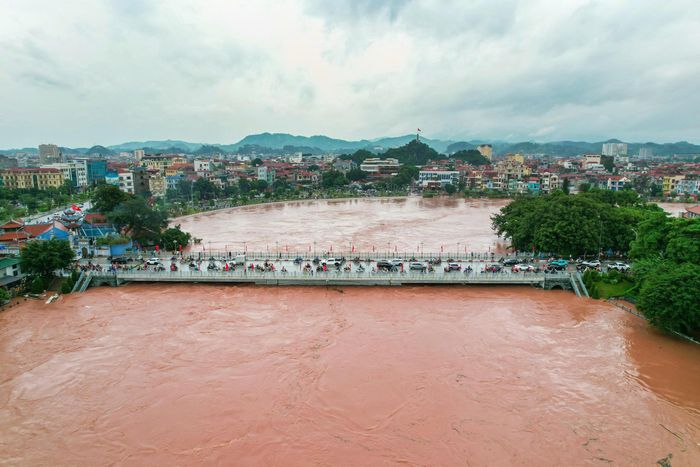 Bất chấp nguy hiểm, nhiều người dân hiếu kỳ tập trung ven sông để quan sát dòng nước lũ cuồn cuộn dâng cao. (Ảnh: Trần Hùng).