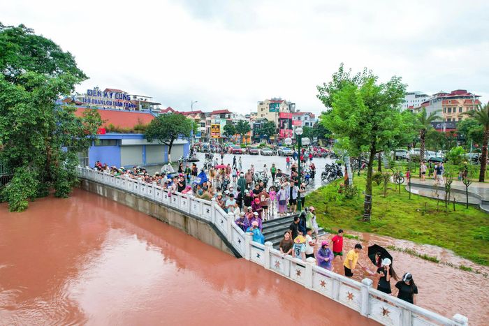 Không ít người đứng trên cầu, sát mép sông để chụp ảnh, quay video và livestream cảnh lũ, tiềm ẩn nguy cơ mất an toàn. (Ảnh: Trần Hùng).