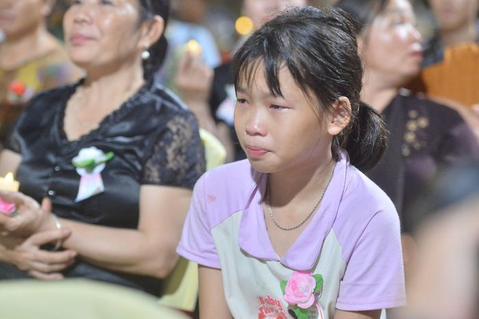 Trên ngực cài bông hồng nhạt, cô bé Bùi Ngọc Linh (10 tuổi) tay cầm ngọn nến nhỏ, bật khóc nức nở.