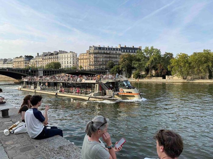 Tàu du lịch trên sông Seine đi qua những khu phố cổ của Paris, trong khi người dân ngồi nghỉ ngay sát mép nước. Ảnh: Hữu Chiến - PV TTXVN tại Pháp