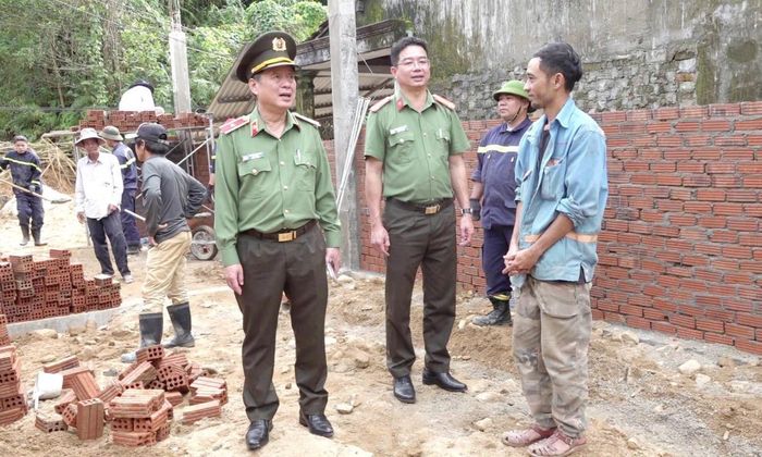 Thiếu tướng Nguyễn Hữu Hợp (trái) động viên người dân vùng lũ đang được lực lượng Công an hỗ trợ xây nhà mới để ổn định cuộc sống.