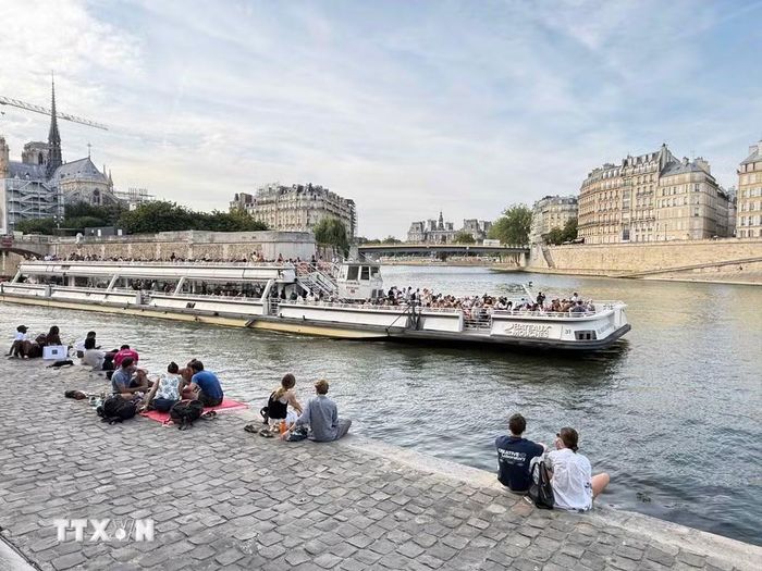 Người dân và du khách ngồi thư giãn bên bờ sông Seine, phía xa là Nhà thờ Đức Bà Paris. (Ảnh: Hữu Chiến/TTXVN)
