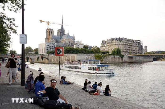 Người dân và du khách ngồi thư giãn bên bờ sông Seine, phía xa là Nhà thờ Đức Bà Paris. (Ảnh: Hữu Chiến/TTXVN)