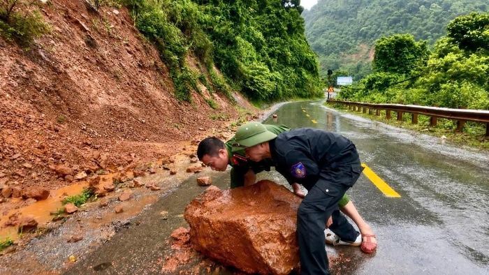 Cán bộ, chiến sĩ Công an xã Nậm Cắn khẩn trương di chuyển tảng đá cùng đất đá ra khỏi mặt đường, góp phần bảo đảm giao thông thông suốt, an toàn. Ảnh: Công an Nghệ An