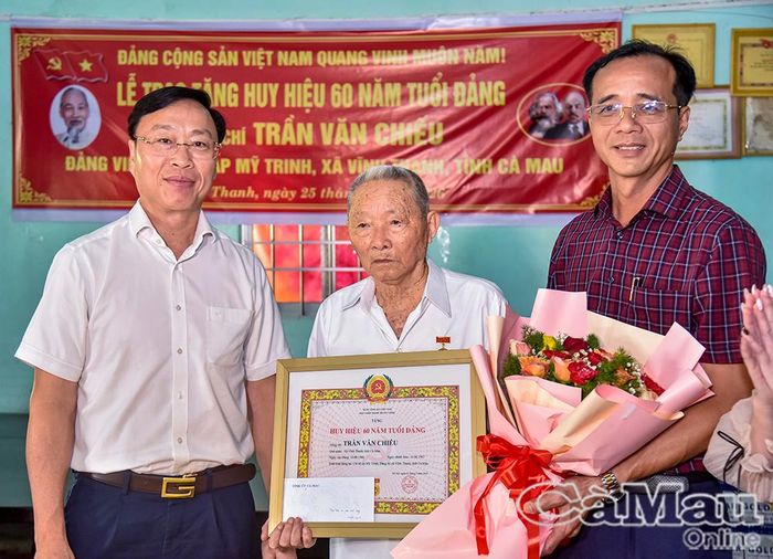 Chủ nhiệm Uỷ ban Kiểm tra Tỉnh uỷ Huỳnh Hữu Trí và Bí thư Đảng uỷ xã Vĩnh Thanh Ngô Nguyên Phong, trao Huy hiệu Đảng và tặng hoa chúc mừng đồng chí Trần Văn Chiếu.