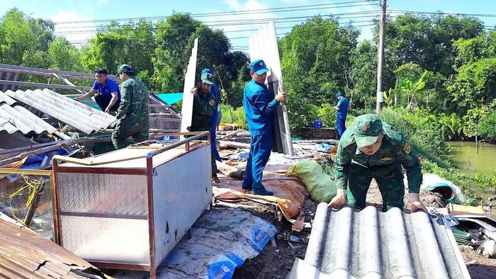 Cán bộ, chiến sĩ Đồn Biên phòng Đất Mũi phối hợp cùng các lực lượng địa phương hỗ trợ vận chuyển mái tôn giúp hộ ông Tâm dựng lại nhà hư hỏng. (Ảnh: Hoàng Tá)