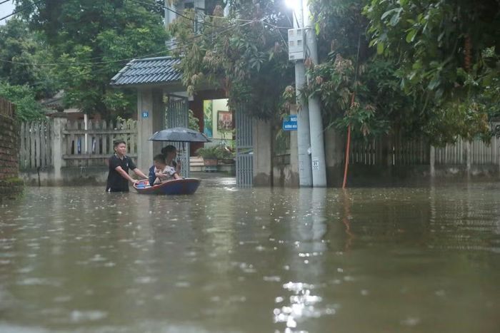 Anh Võ Mạnh Kiên lội dưới dòng nước ngập, đẩy thuyền chở vợ là chị Nguyễn Thị Thu Hương cùng con nhỏ về nhà.