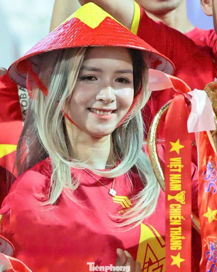 Nữ cổ động viên đội nón lá in hình quốc kỳ, đứng bên mô hình chiếc cúp và dải băng mang thông điệp “Việt Nam chiến thắng”. Trước trận lượt về, thầy trò HLV Kim Sang-sik nắm lợi thế nhờ hai bàn thắng của Hai Long và Quang Hải tại Rajamangala. Ảnh: Như Ý.