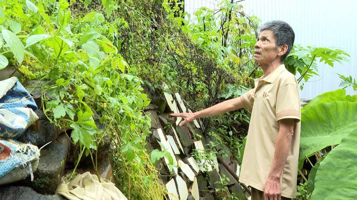 Ông Bùi Quang Thành dùng gạch vụn và đá để gia cố vách tường sau nhà, ngăn đất tràn vào nơi ở mỗi khi trời mưa to (Ảnh: Xuân Trí)