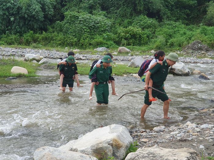 Cán bộ chiến sĩ đồn Biên phòng Trịnh Tường đưa các cháu học sinh qua suối. Ảnh: Trung Dũng