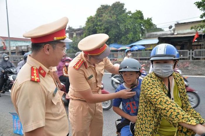 Cảnh sát giao thông tặng mũ bảo hiểm và nhắc nhở người dân tuân thủ việcđội mũ bảo hiểm và cài quai đúng quy cách để đảm bảo an toàn.