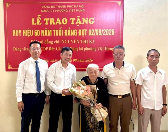 Phó Bí thư Thường trực Đảng ủy phường Việt Hưng Lê Đức Toàn (thứ nhất từ trái qua) trao Huy hiệu 70 năm tuổi Đảng và tặng hoa chúc mừng đảng viên Nguyễn Thị Ký. Ảnh: PV