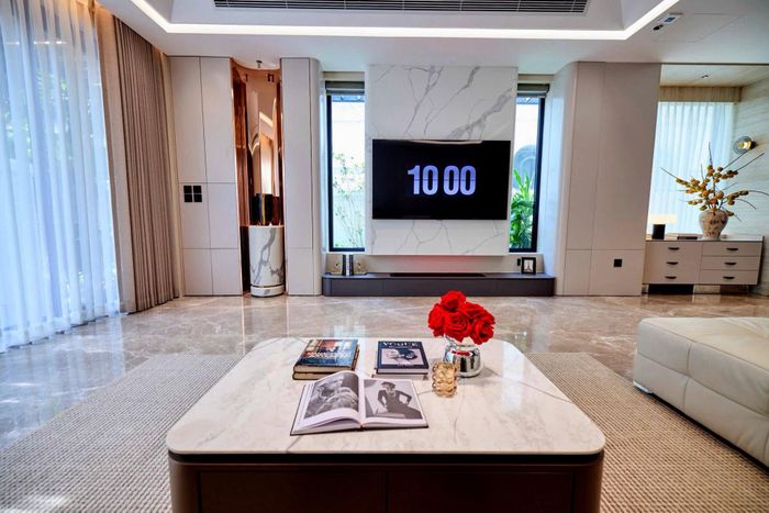 Đối diện sofa là hệ tivi âm tường kích thước lớn. Phía dưới có lò sưởi điện hơi nước, tạo điểm nhấn cho khu vực giải trí của gia đình. Phần tường phía sau sofa được ốp gỗ, giúp tổng thể bớt lạnh và tạo cảm giác ấm cúng hơn. Đồ trang trí không xuất hiện quá dày đặc, chủ yếu là những món có thiết kế đơn giản, phù hợp với phong cách chung của căn phòng.