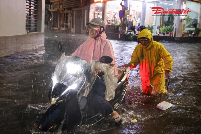Công nhân thoát nước hỗ trợ đẩy xe máy cho người dân qua khu vực nước dềnh sau cơn mưa lớn.