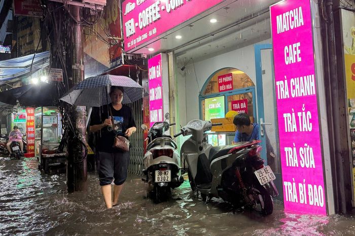  Vỉa hè một số đoạn đường Trần Cung có chiều cao từ 20-30 cm nhưng cũng bị nước ngập đến cao quá mắt cá chân. Anh Tuấn (chủ một cửa hàng kinh doanh đồ uống trên đường Trần Cung) cho biết: "Trận mưa bắt đầu từ khoảng 16h30 và mưa liên tục không dừng khiến nước lên nhanh. Tôi phải tạm nghỉ bán, dùng ván gỗ che chắn trước cửa để tránh nước tràn vào cửa hàng đồng thời dùng xe máy chắn sóng từ ôtô đi qua đánh vỡ cửa kính cửa hàng". Ảnh: Việt Linh. 