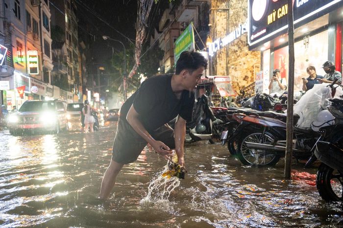  Tại đường Mỹ Đình, nhiều điểm nước ngập khoảng 30 cm. Người dân chủ động vớt rác tại miệng cống để nước thoát nhanh hơn. Ảnh: Viết Huy. 
