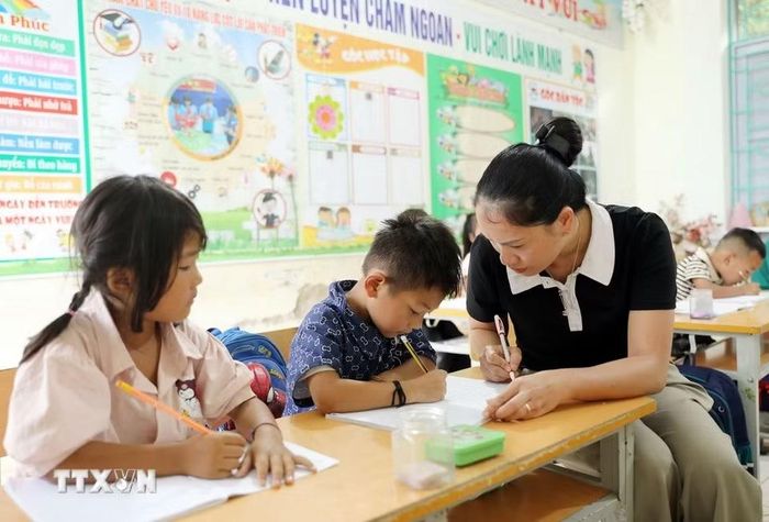 Giáo viên Trường Phổ thông Dân tộc Bán trú Tiểu học và Trung học cơ sở Thu Lũm hướng dẫn học sinh lớp 1 viết chữ trước khi vào năm học mới. (Ảnh: Quý Trung/TTXVN)