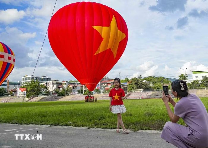 Em nhỏ mặc áo in hình ngôi sao vàng được người thân chụp ảnh lưu niệm bên khinh khí cầu mang Quốc kỳ Việt Nam. (Ảnh: Xuân Tư/TTXVN)