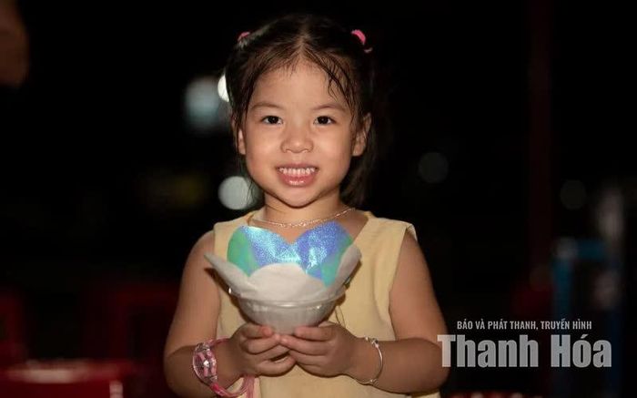 Gương mặt trong veo và ánh nhìn rạng rỡ của em nhỏ bên đài sen - một nét hồn nhiên làm mềm lại cả không gian trầm mặc.