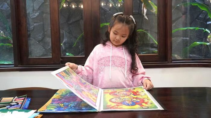 Thiên An bên cuốn tập lưu giữ những bức tranh em tự vẽ. Ảnh: Chu Hằng