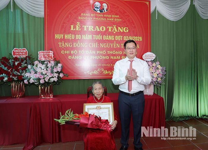 Đồng chí Trần Đăng Quỳnh, Ủy viên dự khuyết Trung ương Đảng, Phó Bí thư Thường trực Tỉnh ủy tặng hoa chúc mừng đồng chí Nguyễn Thị Hòa, đảng viên Chi bộ Tổ dân phố Thống Nhất 1, Đảng bộ phường Nam Định.