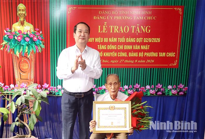 Đồng chí Mai Văn Tuất, Phó Bí thư Tỉnh ủy, Trưởng Đoàn ĐBQH tỉnh trao tặng Huy hiệu 80 năm tuổi Đảng và tặng hoa chúc mừng đồng chí Đinh Văn Nhật, Chi bộ Tổ dân phố Khuyến Công, Đảng bộ phường Tam Chúc.