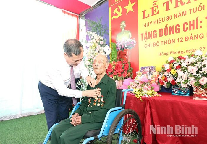 Đồng chí Lê Quốc Chỉnh, Phó Bí thư Tỉnh ủy, Chủ tịch HĐND tỉnh gắn Huy hiệu 80 năm tuổi Đảng cho đồng chí Trần Văn Nghi, đảng viên Chi bộ thôn 12, Đảng bộ xã Hồng Phong.