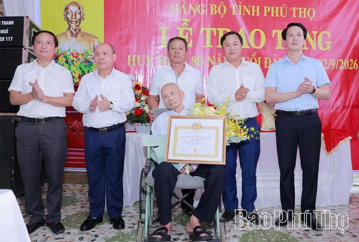 Đồng chí Phó Bí thư Tỉnh ủy, Chủ tịch HĐND tỉnh Bùi Đức Hinh trao Huy hiệu 80 năm tuổi Đảng và tặng hoa chúc mừng đảng viên Nguyễn Văn Phụ.