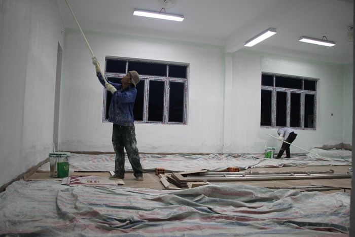 Công nhân tăng ca đêm để sơn phía trong căn phòng học.