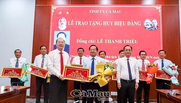 Đồng chí Nguyễn Hồ Hải, Bí thư Tỉnh uỷ và đồng chí Phạm Văn Thiều, Phó Bí thư Tỉnh uỷ, Chủ tịch HĐND tỉnh, trao Khánh vàng, Huy hiệu 35 năm tuổi Đảng và tặng hoa chúc mừng đồng chí Lê Thanh Triều, Uỷ viên Ban Thường vụ Tỉnh uỷ, Phó Chủ tịch Thường trực Uỷ ban MTTQ Việt Nam tỉnh Cà Mau.