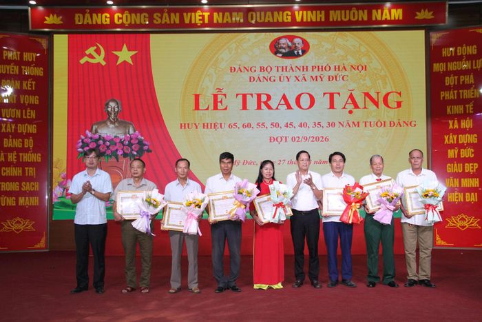 Chủ tịch UBND xã Mỹ Đức Lê Văn Đoàn Phó (ngoài cùng bên trái) và Chủ nhiệm Ủy ban kiểm tra Đảng ủy xã Mỹ Đức Mai Thành Công (thứ 4 từ phải qua) trao Huy hiệu Đảng tặng đảng viên. Ảnh: Biên Phạm