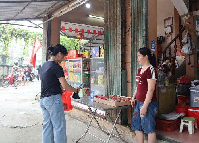 Người dân xã Hát Môn quét mã thanh toán không dùng tiền mặt khi mua hàng tại chợ Hát. Ảnh: NM