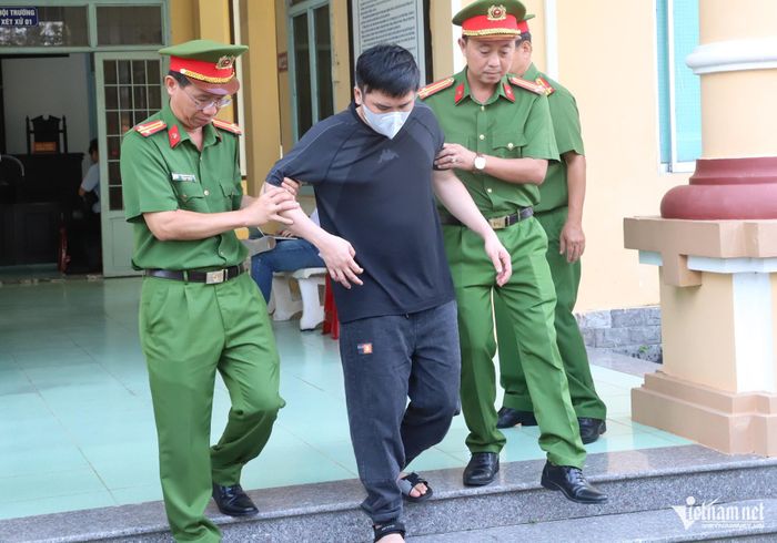 Bị cáo Nguyễn Văn Bảo Trung đi cà nhắc, được lực lượng công an dìu xuống bậc thang. 