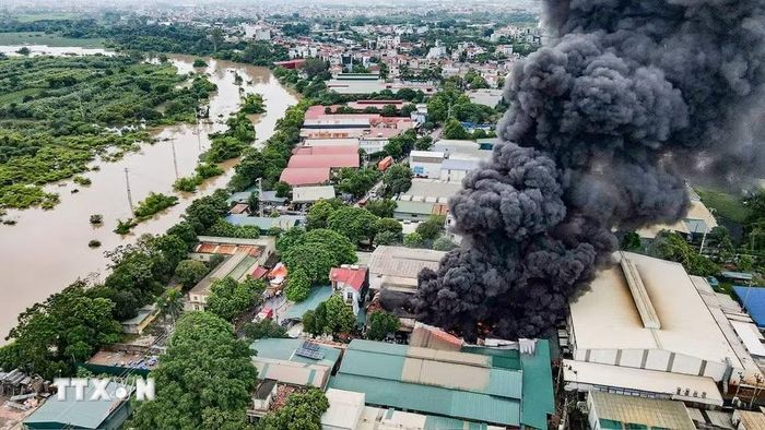 Lửa và khói đen bốc lên tại khu xưởng nằm gần nhiều nhà xưởng, công trình và khu dân cư, tiềm ẩn nguy cơ cháy lan. (Ảnh: TTXVN phát)