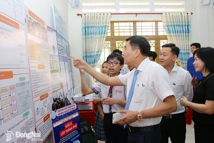 Phó Bí thư Đảng ủy, Chủ tịch UBND phường Trảng Bom Lê Ngọc Tiên nghe các học sinh của phường giới thiệu các mô hình sáng chế đạt giải cao tại cuộc thi khoa học, kỹ thuật cấp thành phố năm học 2025-2026 tại buổi lễ công bố. Ảnh: Hải Quân