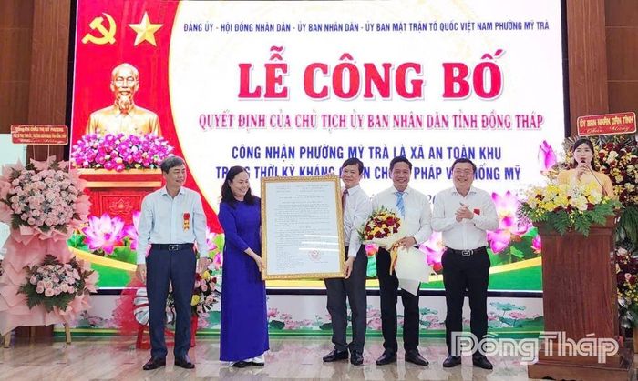 Đồng chí Phạm Văn Chuẩn (bìa trái) trao Quyết định của Chủ tịch UBND tỉnh Đồng Tháp về việc công nhận Mỹ Trà là phường An toàn khu và đồng chí Phan Văn Thương tặng hoa chúc mừng. Ảnh: PHAN AN
