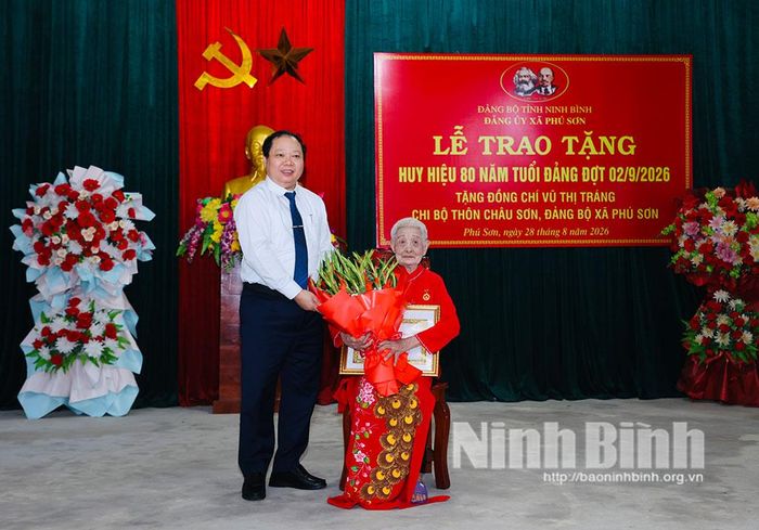 Đồng chí Vũ Hồng Hiên, Ủy viên Ban Thường vụ Tỉnh ủy, Chủ nhiệm Ủy ban Kiểm tra Tỉnh ủy tặng hoa chúc mừng đồng chí Vũ Thị Tráng, đảng viên Chi bộ thôn Châu Sơn, Đảng bộ xã Phú Sơn.