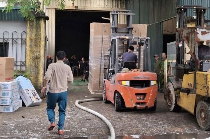 Lực lượng chức năng cùng người dân di chuyển hàng hóa ra khỏi kho xưởng bị cháy. Ảnh: NDCC