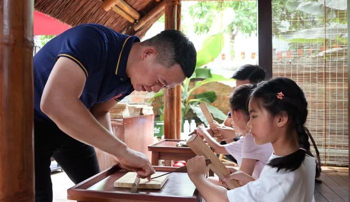 Nghệ nhân Bùi Quân tận tình hướng dẫn các “nghệ nhân nhí” thực hành các kỹ thuật đục chạm gỗ truyền thống. (Ảnh: Fanpage Văn Miếu)