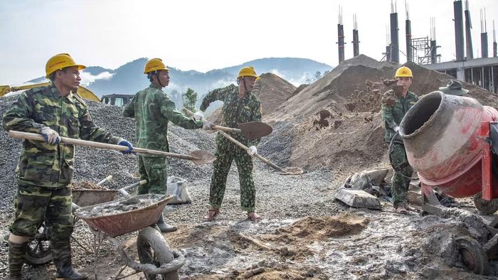 Trung tá Zơ Râm Thân (thứ nhất từ trái sang) cùng đồng đội trộn bê tông. Phía xa xa thấp thoáng những ngọn núi trong dãy Trường Sơn Ảnh: Lê Văn Chương