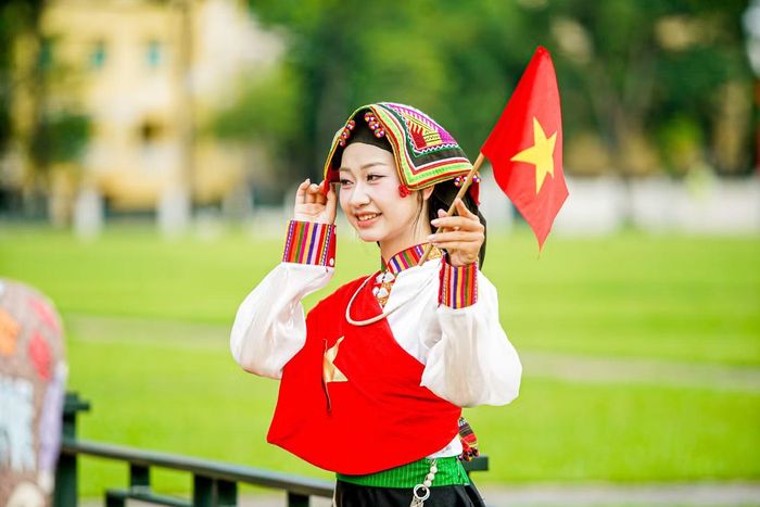 Thiếu nữ tạo dáng với trang phục dân tộc và cờ đỏ sao vàng.