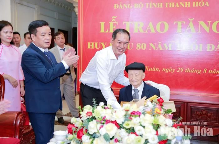 Phó Bí thư Tỉnh ủy Trịnh Tuấn Sinh trao Huy hiệu 80 năm tuổi Đảng và tặng hoa chúc mừng đảng viên Nguyễn Ngọc Chinh.