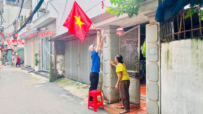 Một cụ bà đứng trước cửa nhà hướng dẫn bạn trẻ treo cờ ngay ngắn. Ảnh: PV