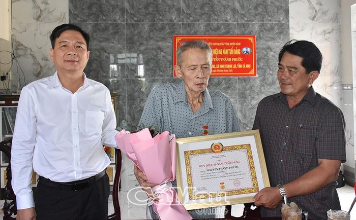  Đồng chí Nguyễn Bình Tân và  đồng chí Lê Hoàng Phi trao Huy hiệu 60 năm tuổi Đảng và tặng hoa chúc mừng đảng viên Nguyễn Thành Phước.