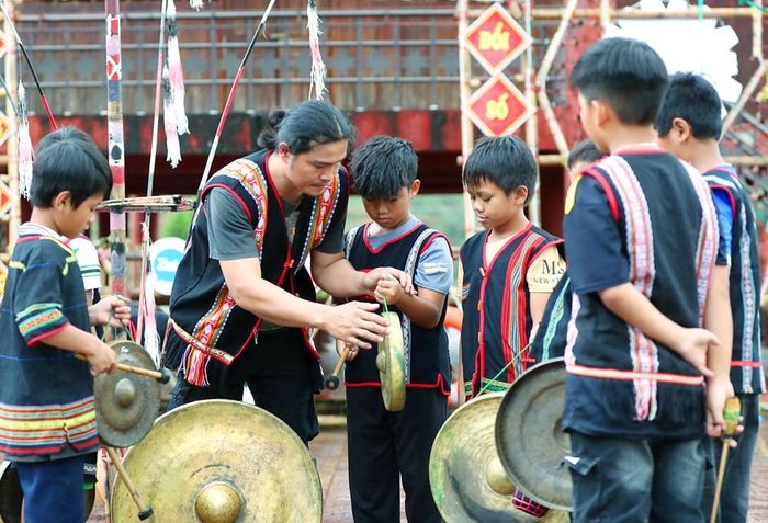 Nghệ nhân A Nai Sưl lắng nghe từng nhịp chiêng, kiên nhẫn hướng dẫn học sinh làm quen với nhạc cụ dân tộc