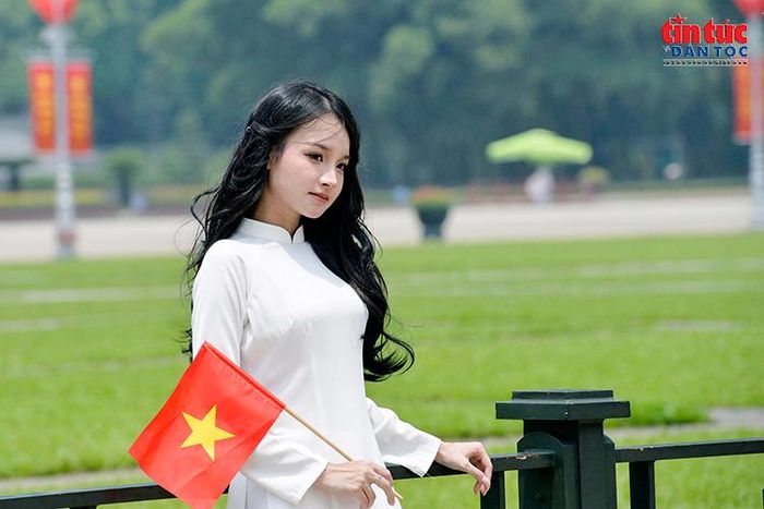 Thiếu nữ duyên dáng trong tà áo dài trắng bên lá cờ đỏ sao vàng.