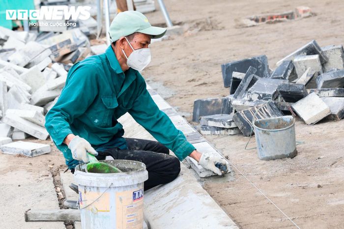 Một số đoạn vỉa hè đang được lát đá, trong khi tại tường chắn, công nhân đục lỗ để phục vụ lắp đặt lan can.